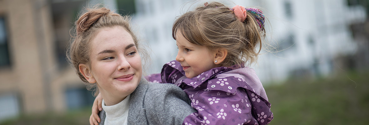 Junge Mutter mit einem Mädchen auf dem Rücken